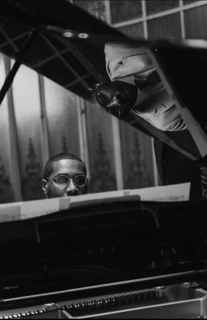 Trevor seated at a grand piano, his face reflected in the raised lid